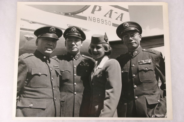 1953 Pan Am stewardess  posing with 3 men in uniform with a Boeing 377 Stratocruiser in the background.